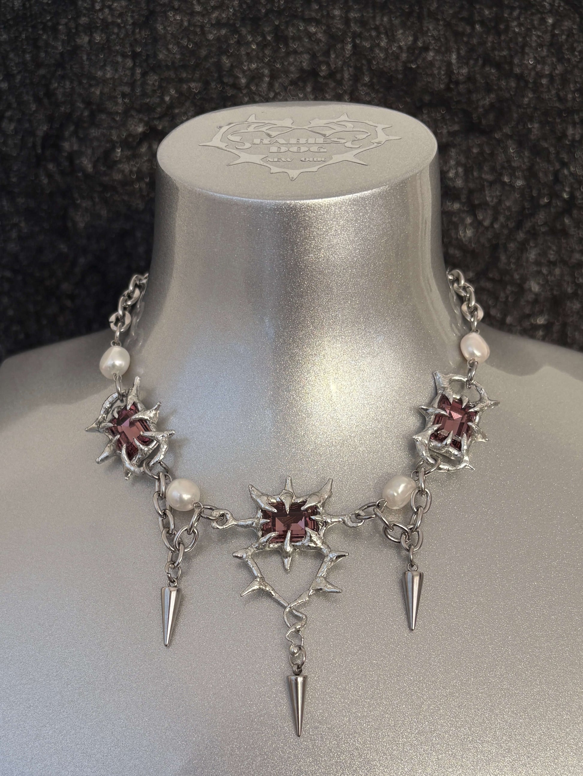 The Midnight Candelabrum Necklace is a sculptural statement piece inspired by gothic candleholders and nocturnal ritual objects. Handcrafted by RABIES DOG, this necklace carries a dark, altar-like presence—designed to be worn as both adornment and symbol.